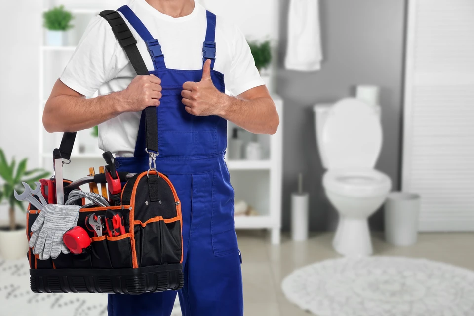 Plombier professionnel en tenue de travail bleue effectuant une réparation sous un évier de cuisine moderne