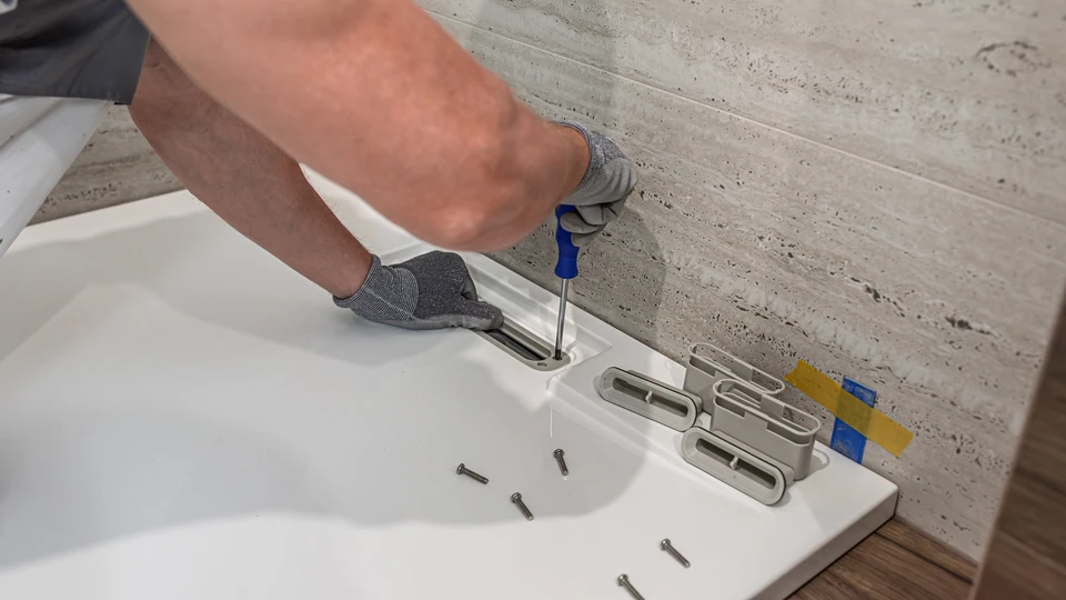 Deux plombiers en salopette bleue et casquette installent un lavabo vasque rond blanc sur plan de travail bois dans une salle de bain moderne