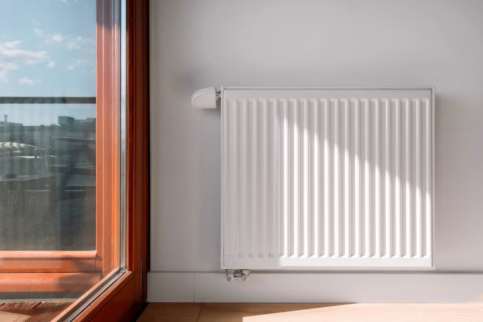 Intérieur résidentiel avec radiateur en fonte blanc installé sous une fenêtre, parquet en bois naturel, murs blancs et encadrement gris