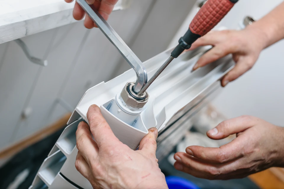 Intérieur résidentiel, mains masculines utilisant une clé à molette pour installer ou régler une vanne thermostatique de radiateur blanc fixé au mur